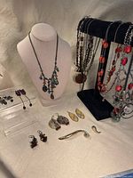 Full lot view of over 10 pieces of vintage jewelry including necklaces, earrings, and brooches arranged on display stand and flat surface.