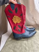 Side view of the red leather cowboy boot shaft with yellow rose and green leaf appliqué, and blue foot and heel.