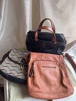 Overview of three purses together; tan Fossil purse, black leather handbag, and patterned fabric purse