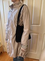 Side view of light beige Lululemon jacket being worn along with black knit purse over shoulder showing length and fit.