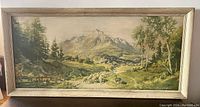 Full view of framed lithograph showing mountain scene with trees and sheep in pasture under glass in beige wooden frame.