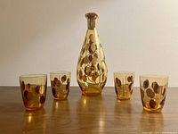 Front view of the amber glass decanter and four matching glasses with gold leaf or floral decoration on a plain white background.
