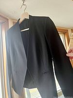 Black Theory blazer front view hanging on hanger showing solid black color and slim pocket detail