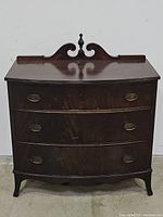 Front view of the antique mahogany bowfront chest showing the three drawers with brass handles and decorative top.