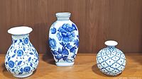 All three blue and white porcelain vases displayed side by side on a wooden surface against a wooden background.
