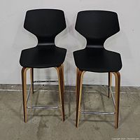 Full front view of two black counter stools side by side showing the shape and design of the seats, legs and footrests.