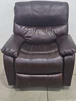 Front view of brown leather recliner chair in upright position on concrete floor against white wall.