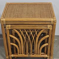 Three rattan and wicker nesting tables stacked one inside the other showing curved and knotted rattan sides and woven wicker tabletops.