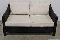 Front view of dark brown multi-tone outdoor wicker loveseat with beige cushions.