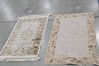 Two rectangular rugs on a concrete floor. Right rug is neutral sage center with taupe floral patterned border. Left rug has intricate floral pattern with fringes.
