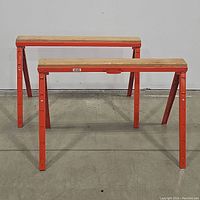 Two steel saw horses with wooden tops placed on a concrete floor seen from front and side angle.