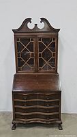 Front view of closed mahogany slant front secretary desk with decorative upper glass cabinet and curved drawers below, showing full height and style.
