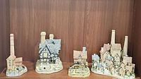 Four hand painted David Winter miniature cottages displayed on wooden shelf showing varied chimneys and textured roof tiles.