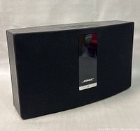 Angled front view showing black fabric grille, Bose logo, and display screen in center.