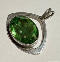 Top view of triangular sterling silver pendant with bezel-set green faceted oval gemstone, showing the polished silver and gemstone details.