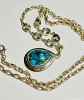 Necklace laid out showing chain and turquoise pendant with clear gemstones.