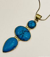 Close-up of turquoise pendant showing three stones in silver bezel setting and chain.
