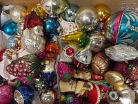 Top-down view of a box filled with assorted vintage and antique glass Christmas tree ornaments in various shapes and colors including globes, Santa heads, and pinecone shapes.