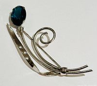Oblique view of the brooch showing the silver curls and blue gemstone