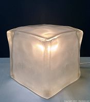 Front view of the lamp illuminated showing frosted, textured translucent glass shaped like an ice cube.
