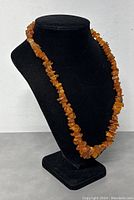 Front view of natural raw amber necklace displayed on black stand, showing the entire length and natural varying amber colors and shapes.