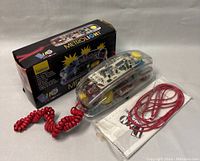 Photo shows the transparent Metrolight telephone with visible internal components, coiled handset cord, straight line cord, and instruction manual beside the original box