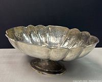Side angle view of vintage silver plated fruit bowl showing scalloped edges and round footed base with ribbed detail.