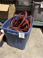 Blue plastic bin containing six automotive booster cables with red and black wires and metal clamps.