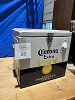 Front and side view of closed Corona Extra cooler box with logo, bottle opener, and latch closure visible.