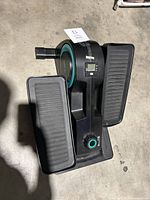 Top and side views of Cubii under desk elliptical showing textured foot pedals, digital display, resistance knob, and Cubii logo.