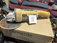 Full view of used yellow DeWalt corded angle grinder resting on a cardboard box, displaying body, handle, and disc guard.