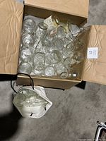 Box filled with multiple clear glass jars of different sizes and shapes, including mason jars and regular glass jars.