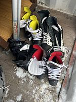 Photo showing six pairs of used hockey skates with different colors and interior padding, arranged on a floor near a metal table leg.