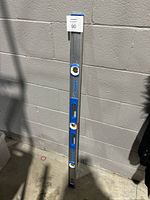 Full view of the Empire aluminum spirit level standing against a wall showing its length and general condition.