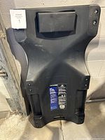 Top view of black plastic automotive creeper showing padded headrest and contoured shape.