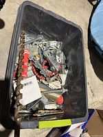 Plastic bin filled with assorted metal hardware including screws, bolts, brackets, washers, and other pieces