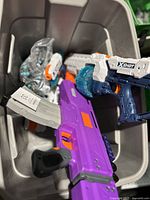 Lot of toy blasters and accessories inside a plastic bin.