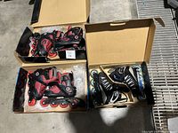 Three pairs of inline roller blades in their original boxes on a floor.