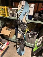 Full view of the Roxy Silhouette snowboard standing upright, showing the graphic top surface, bindings, and attached straps.