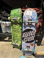 Photo of bottom side of two skateboards, one green Creature board and one blue/pink Santa Cruz board showing graphic designs and wear