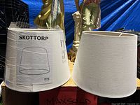 Two Skottorp lamp shades, one unpackaged and one still sealed in plastic IKEA packaging, displayed side-by-side