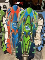 Four Body Glove snow sleds in various colors: green/blue, orange/blue, green/black, and blue/black, stacked against a shelf.
