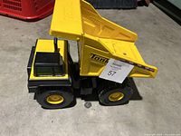 Side view of yellow and black Tonka metal dump truck toy with dump bed raised showing wear consistent with normal use