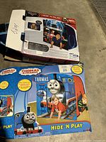 Box front showing the Thomas & Friends Hide 'N Play pop up tent with Thomas the Tank Engine graphics and a child playing in the tent.