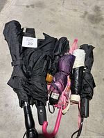 Multiple umbrellas of various colors and sizes arranged on the floor, mostly folded and grouped together.