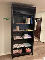Front view photo of black wooden bookshelf with items on shelves for scale and condition check
