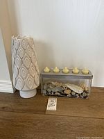 Full view showing the metal and glass candle holder containing shells and six small candles along with the white ceramic floor vase with an embossed pattern standing beside it.