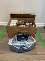Sanyo portable CD/FM player sitting in front of a large bankers box full of CDs, showing the entire lot.