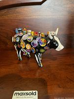 Photo showing black and white ceramic cow figurine covered in miniature colorful hand painted ceramic dishes and kitchenware items on a wooden surface.