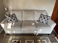 Front view of cream coloured three-seater couch with two patterned throw pillows on a floral rug.